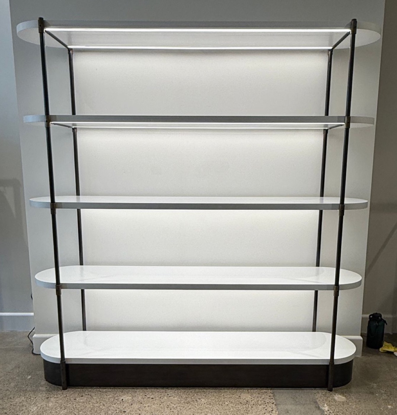 Five-tier display shelving with white oval shelves on dark metal posts, lit from behind